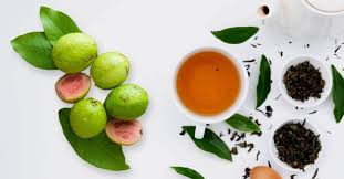 Fresh green limes, tea cup, loose tea leaves, and spices for guava leaf tea preparation.