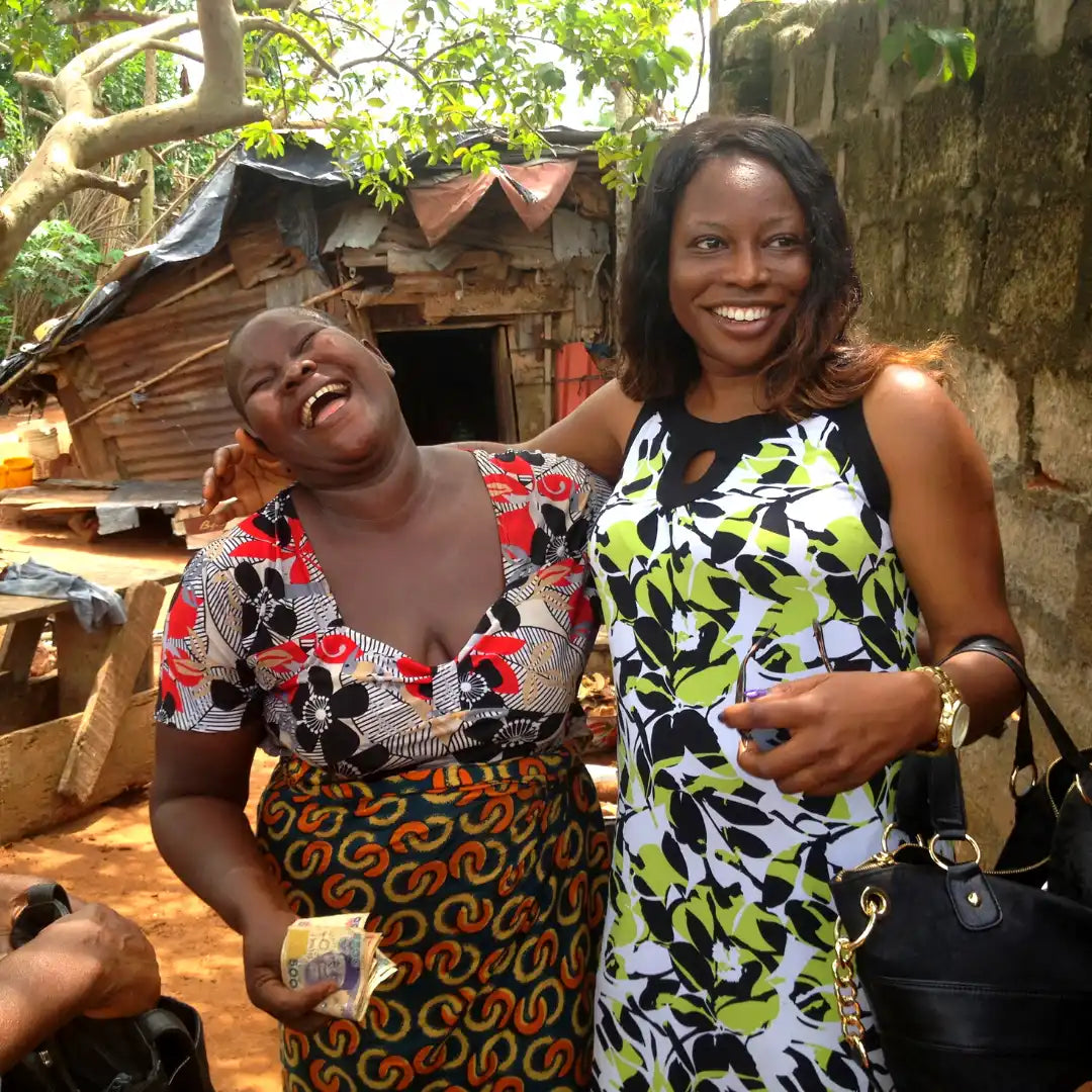 Two people wearing colorful patterned dresses share a joyful moment outdoors.